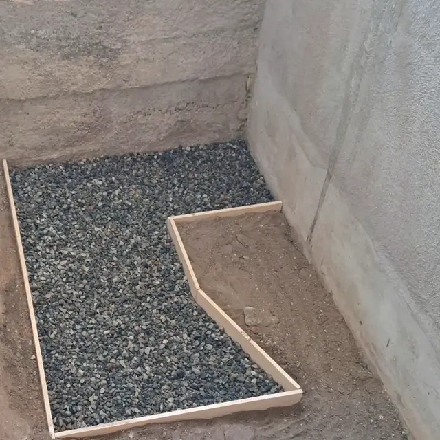 Coffrage en bois et lit de gravier préparant la petite dalle sous une future douche